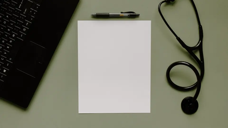 A stethoscope, a pen and a blank sheet of paper on a desk