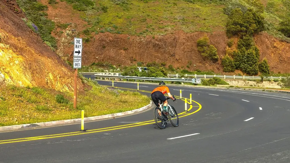 A cyclist riding along a curved road marked with yellow center lines
