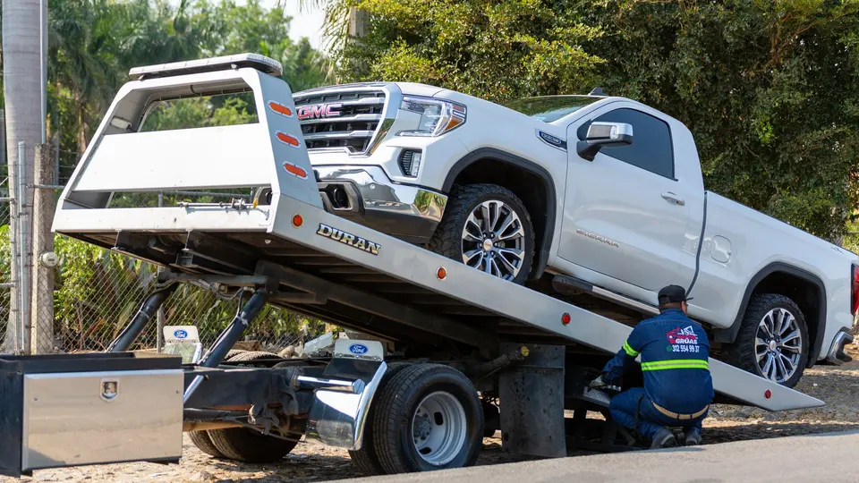 A tow truck operator loading a white pickup onto a flatbed at the roadside after a crash