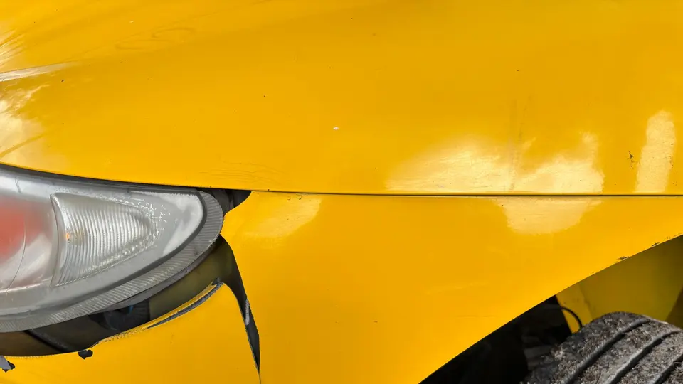 Close-up of a yellow car's front bumper and headlight damaged in a collision