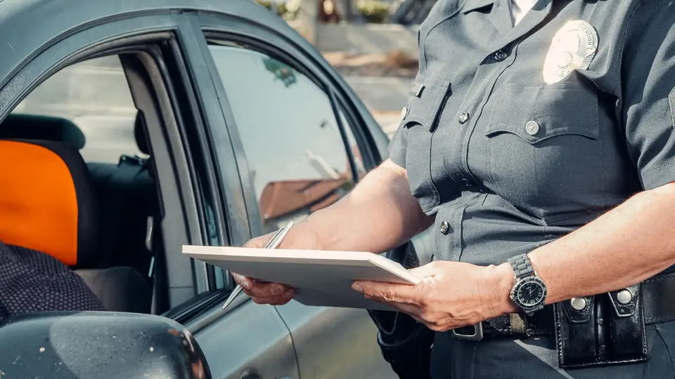 A police officer in uniform holding a tablet beside a car window while taking a report