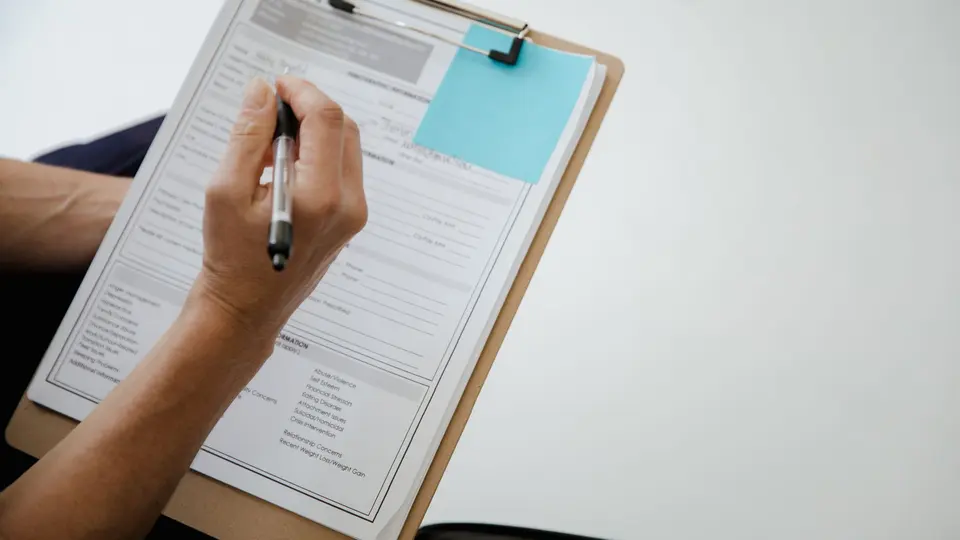 A hand writing on a paper form attached to a clipboard