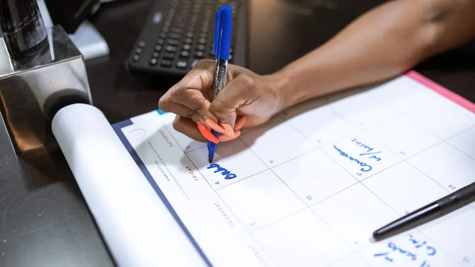 A hand writing a date on a desk calendar with a blue pen