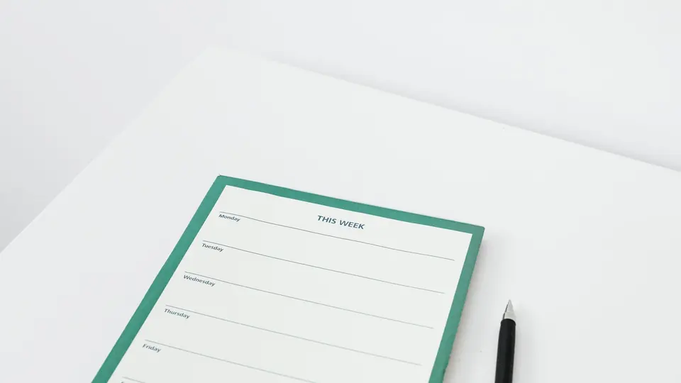 A blank weekly planner pad and a pen on a white desk