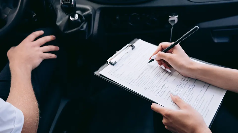 Hands filling in an insurance claim form on a clipboard inside a vehicle