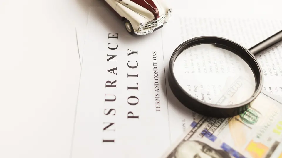 An insurance policy document with a magnifying glass, a toy car and U.S. dollar bills